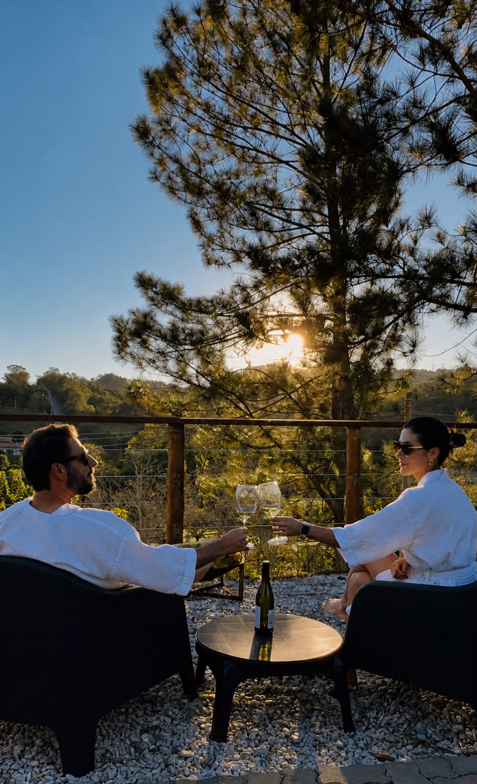 Casal brindando com taças de vinho no deck durante o pôr do sol